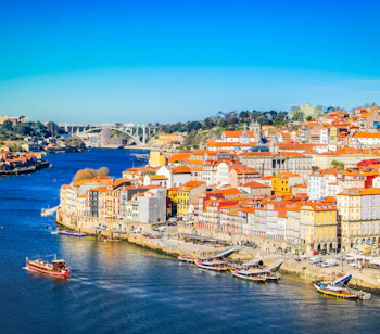 Farverig udsigt over Portos historiske Ribeira-kvarter langs Douro-floden med traditionelle både og røde tagtegl i solskin