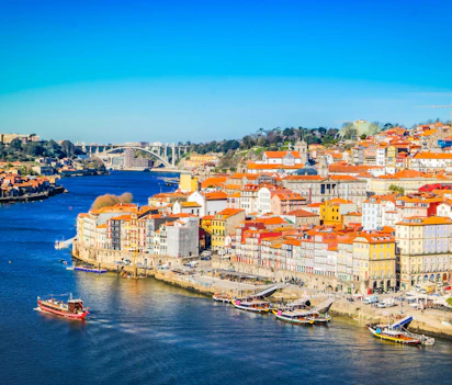 Farverig udsigt over Portos historiske Ribeira-kvarter langs Douro-floden med traditionelle både og røde tagtegl i solskin