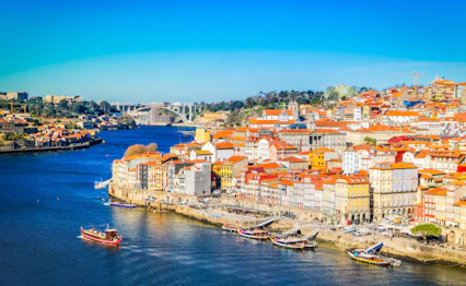 Farverig udsigt over Portos historiske Ribeira-kvarter langs Douro-floden med traditionelle både og røde tagtegl i solskin