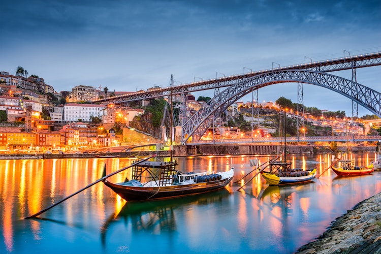 Porto byens smukke skyline ved aftentid med traditionelle Rabelo-både på Douro-floden, der historisk transporterede portvin