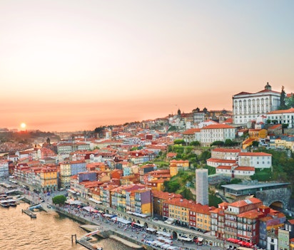 Betagende udsigt over Portos historiske centrum ved solnedgang med farverige bygninger langs Douro-floden og Porto Katedralen på bakketoppen