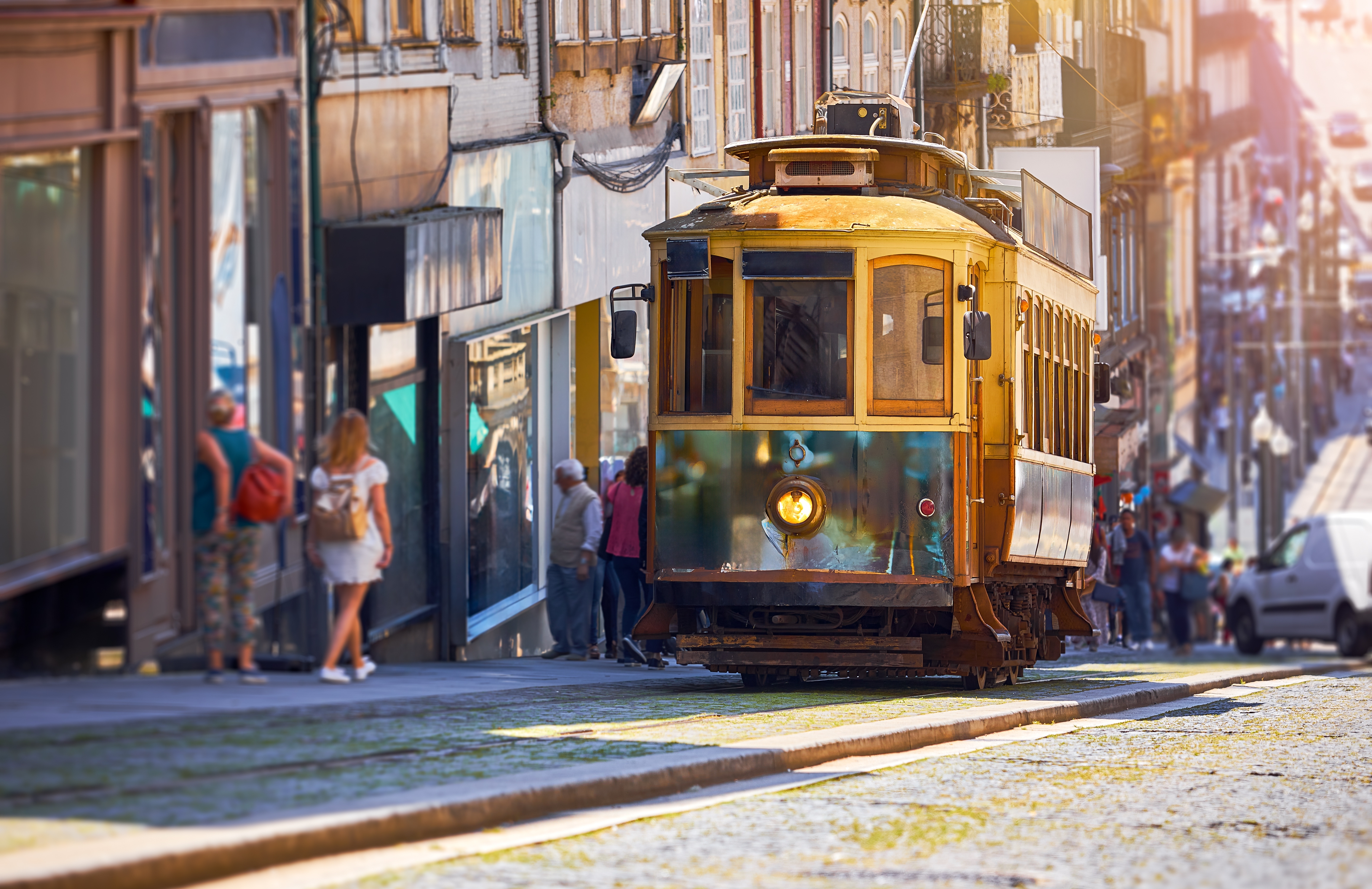 Klassisk gul sporvogn kører gennem Portos historiske gader i det gyldne solnedgangslys, et ikonisk symbol på den portugisiske bys charmerende transportmiddel