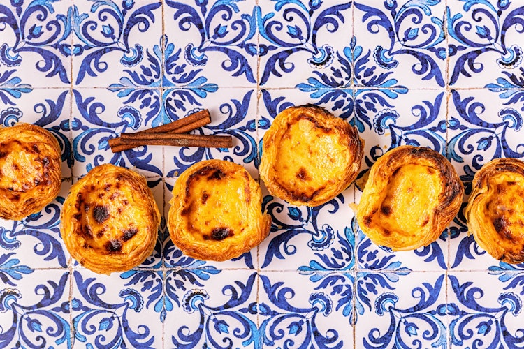 Traditionel portugisisk æggetærte Pastel de Nata på blå azulejo-flise baggrund, en berømt dessert fra Lissabon som du kan smage på vores rundrejse