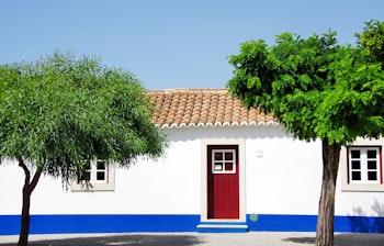 Traditionelt hvidt portugisisk hus med rød dør og teglstenestag i Porto Covo landsby