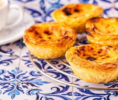 Traditionel portugisisk pastel de nata æggetærte med sprød skorpe og cremet fyld, serveret mod blå azulejo-fliser i Lissabon