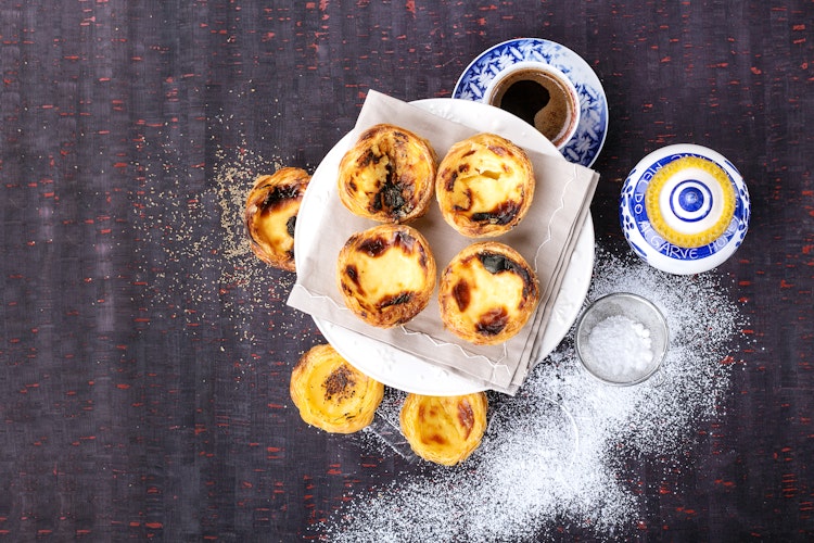 Traditionel portugisisk Pastel de Nata serveret med kaffe og honning på træbakke i Lissabon, perfekt til at nyde under din rejse til Portugal