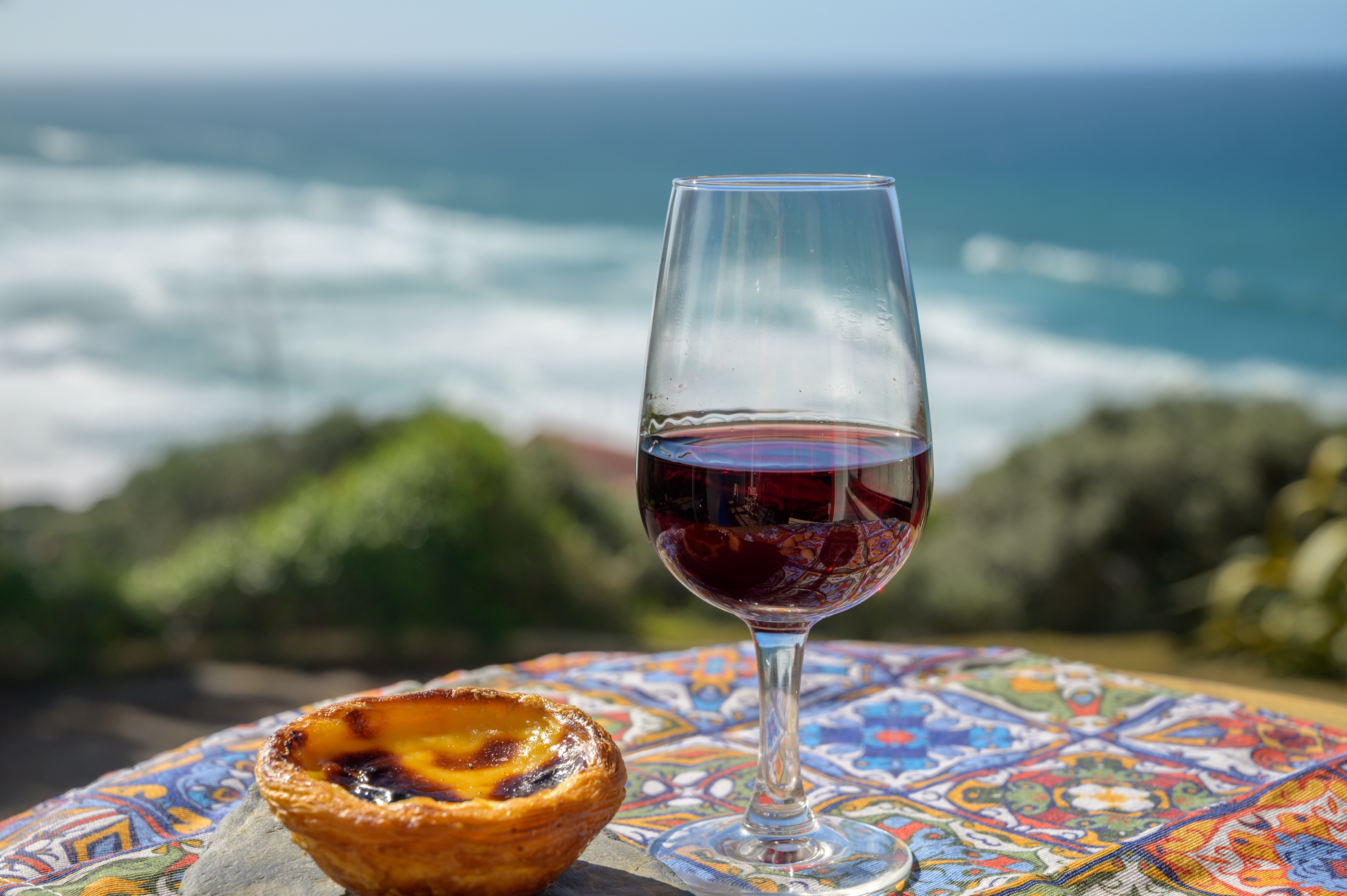 Traditionel portugisisk Pastel de Nata æggetærte og portvin med udsigt over Atlanterhavet nær Sintra i Portugal