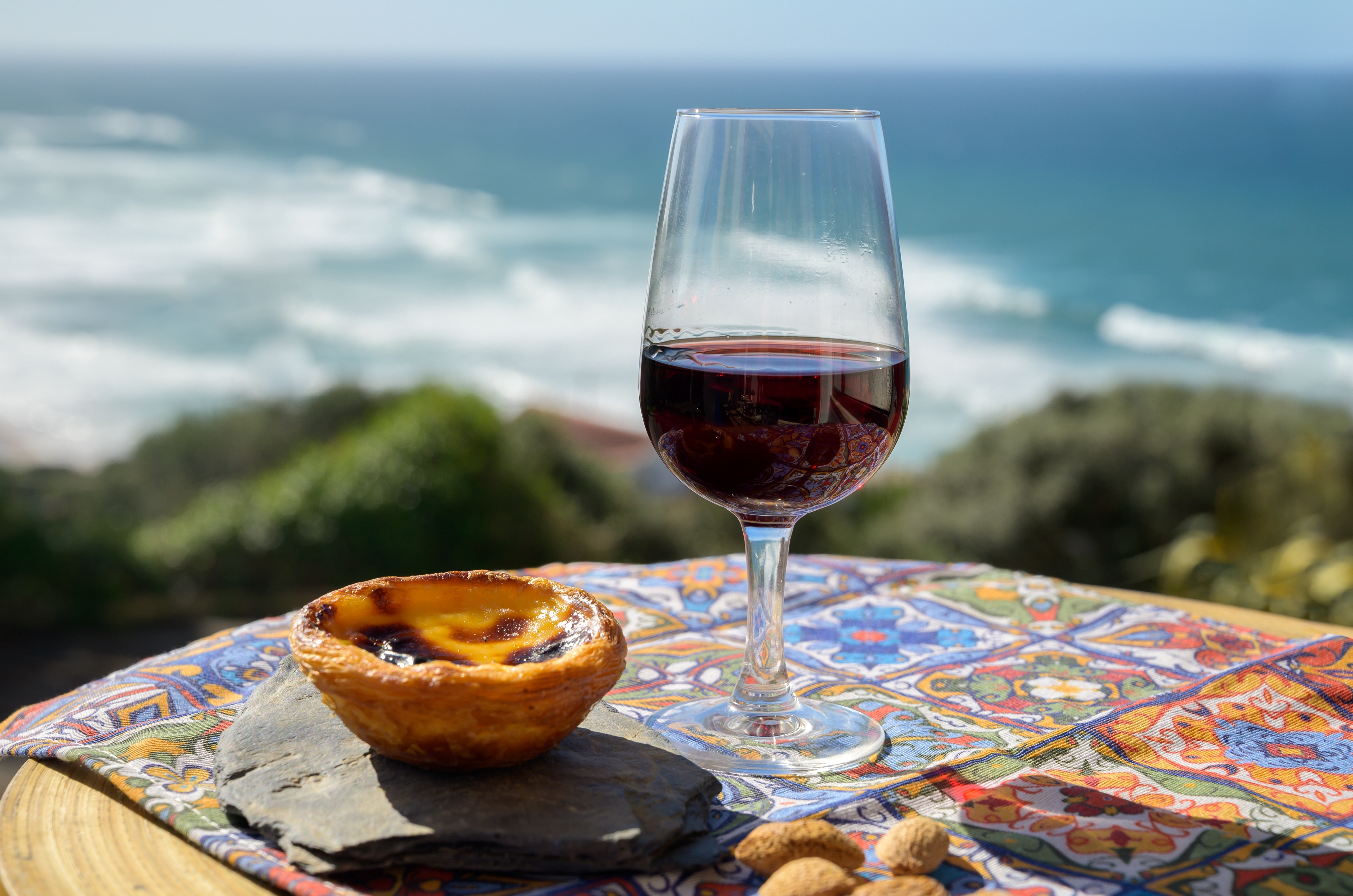 Traditionel portugisisk Pastel de Nata og et glas rødvin nydes med udsigt over Atlanterhavet i Cascais