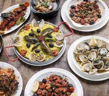 Autentisk portugisisk tapas-udvalg med friske skaldyr, grillet kød, risretter og forskellige tilbehør serveret på et rustikt træbord