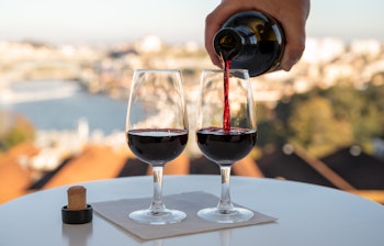 Servering af ruby portvin i glas med udsigt over Douro-floden og Porto by i solnedgang fra Vila Nova de Gaia