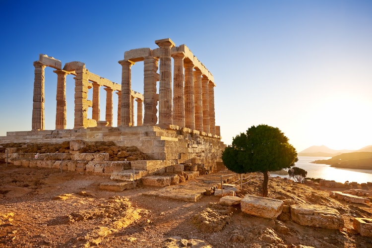 Det antikke Poseidon tempel på Kap Sounion i Grækenland badet i gyldent solnedgangslys, med majestætiske doriske søjler der troner over Det Ægæiske Hav fra sin dramatiske placering på klippetoppen.