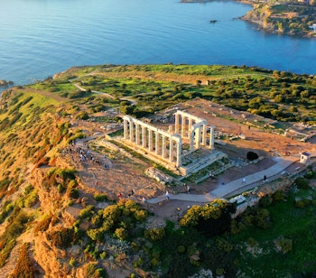 Luftfoto af det antikke Poseidon-tempel på Kap Sounion med de karakteristiske søjler på klippetop med panoramaudsigt over Det Ægæiske Hav i solnedgangen