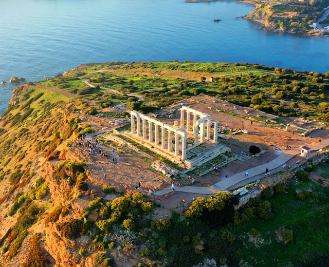 Luftfoto af det antikke Poseidon-tempel på Kap Sounion med de karakteristiske søjler på klippetop med panoramaudsigt over Det Ægæiske Hav i solnedgangen