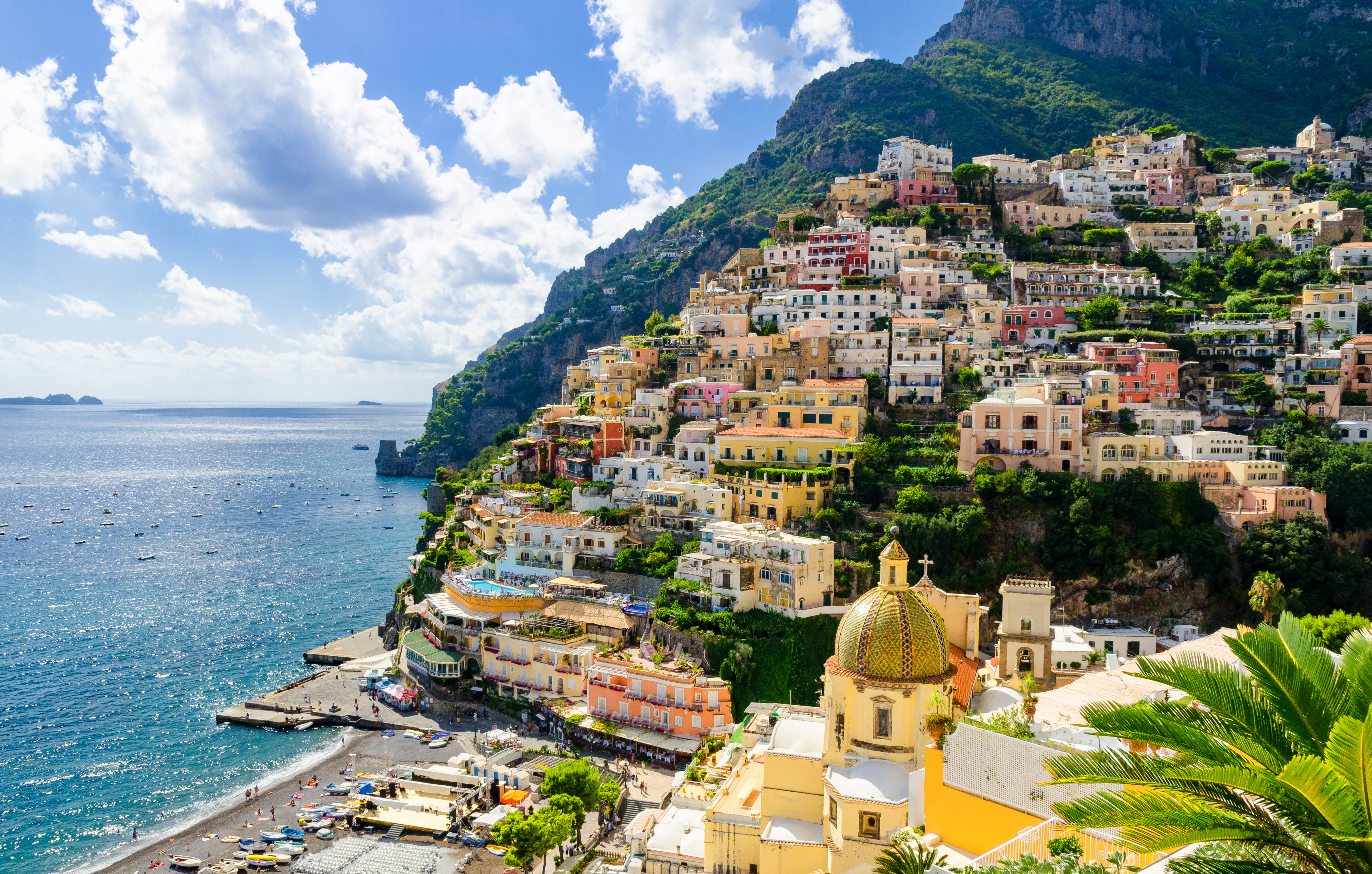 Smuk udsigt over Positanos farverige huse på klippeskråninger langs Amalfi-kysten med tyrkisblåt middelhav og historisk kirke