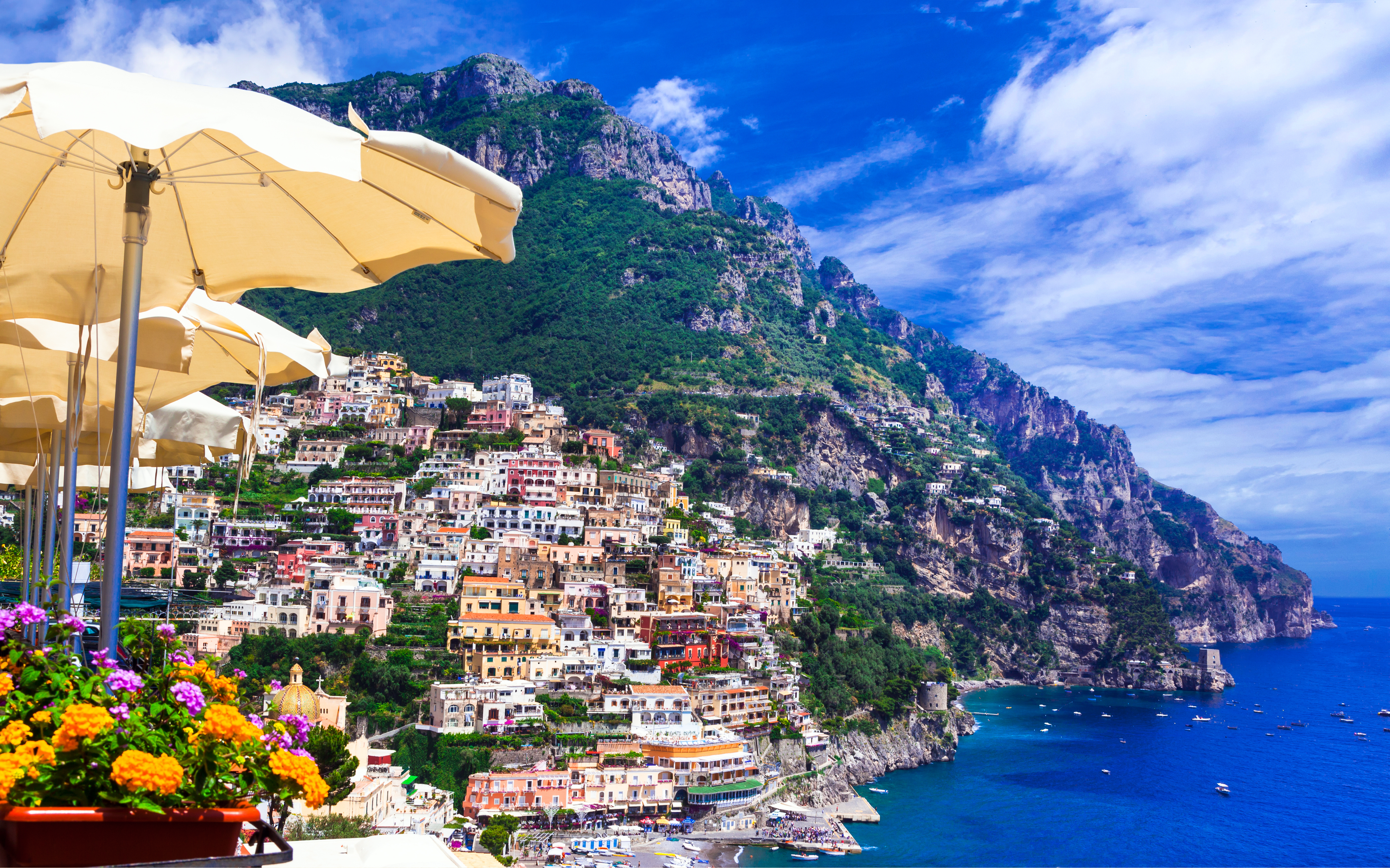 Betagende panoramaudsigt over Positano på Amalfikysten med farverige bygninger, der falder ned mod det turkisblå Middelhav, perfekt eksempel på luksuriøse italienske kystferier