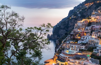 Betagende panoramaudsigt over Positano på Amalfikysten i Campania, Italien, med farverige huse der kaskader ned ad de stejle klipper mod det turkisblå Middelhav i solnedgangens gyldne lys