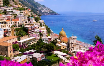 Malerisk panoramaudsigt over Positano med farverige bougainvillea-blomster, terrasserede bygninger og det blå Middelhav på Amalfikysten i Italien