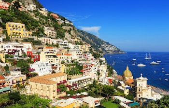 Betagende udsigt over Positano med farverige bygninger, der falder ned ad klipperne ved Amalfi-kysten i Italien med det turkisblå Middelhav i forgrunden