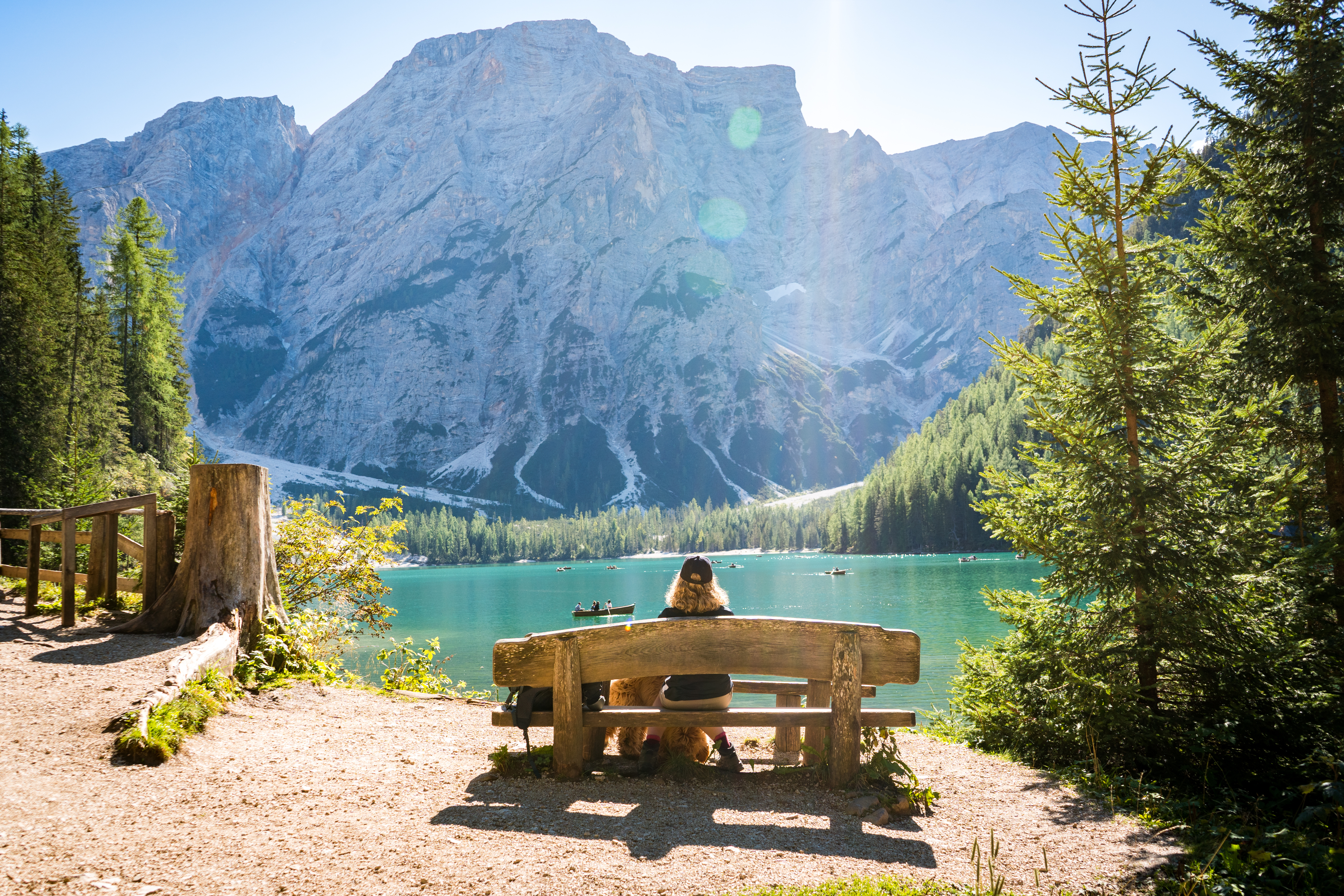 Ung kvinde sidder på en rustik træbænk med udsigt over den turkisblå Pragser Wildsee sø omgivet af fyrreskov og dramatiske Dolomit-bjerge i Sydtyrol, Italien