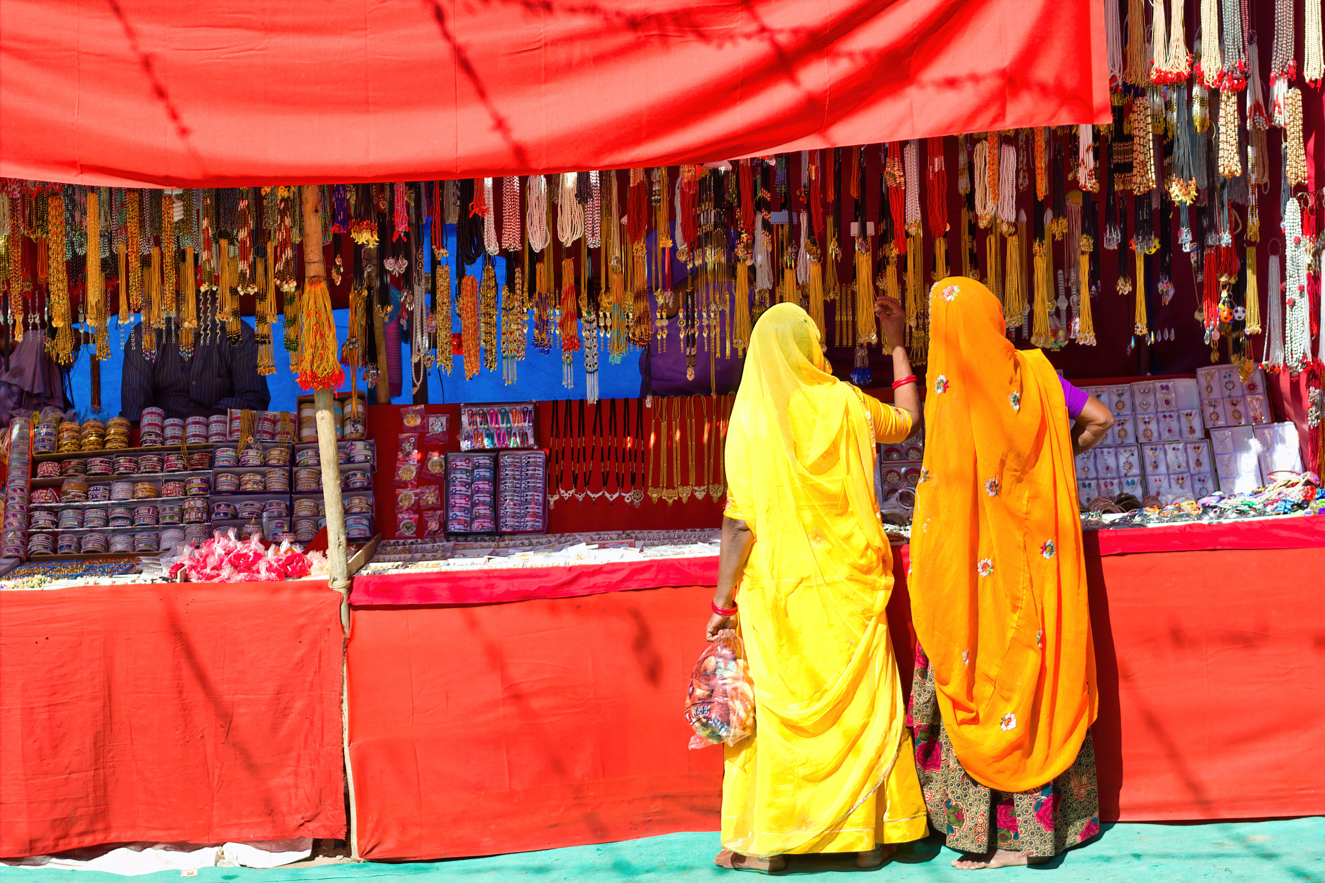 Kvinder i farverige traditionelle sarees køber smykker ved en markedsbod under den berømte Pushkar-messe i Rajasthan, Indien - et fascinerende indblik i lokal kultur og handelstraditioner