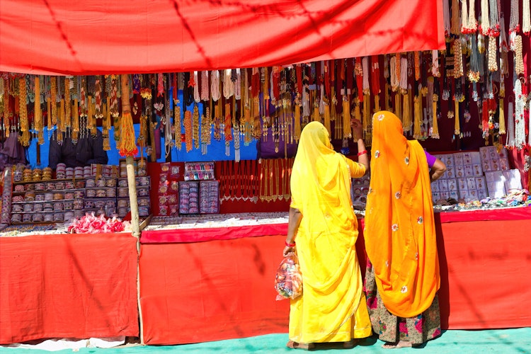 Kvinder i farverige traditionelle sarees køber smykker ved en markedsbod under den berømte Pushkar-messe i Rajasthan, Indien - et fascinerende indblik i lokal kultur og handelstraditioner