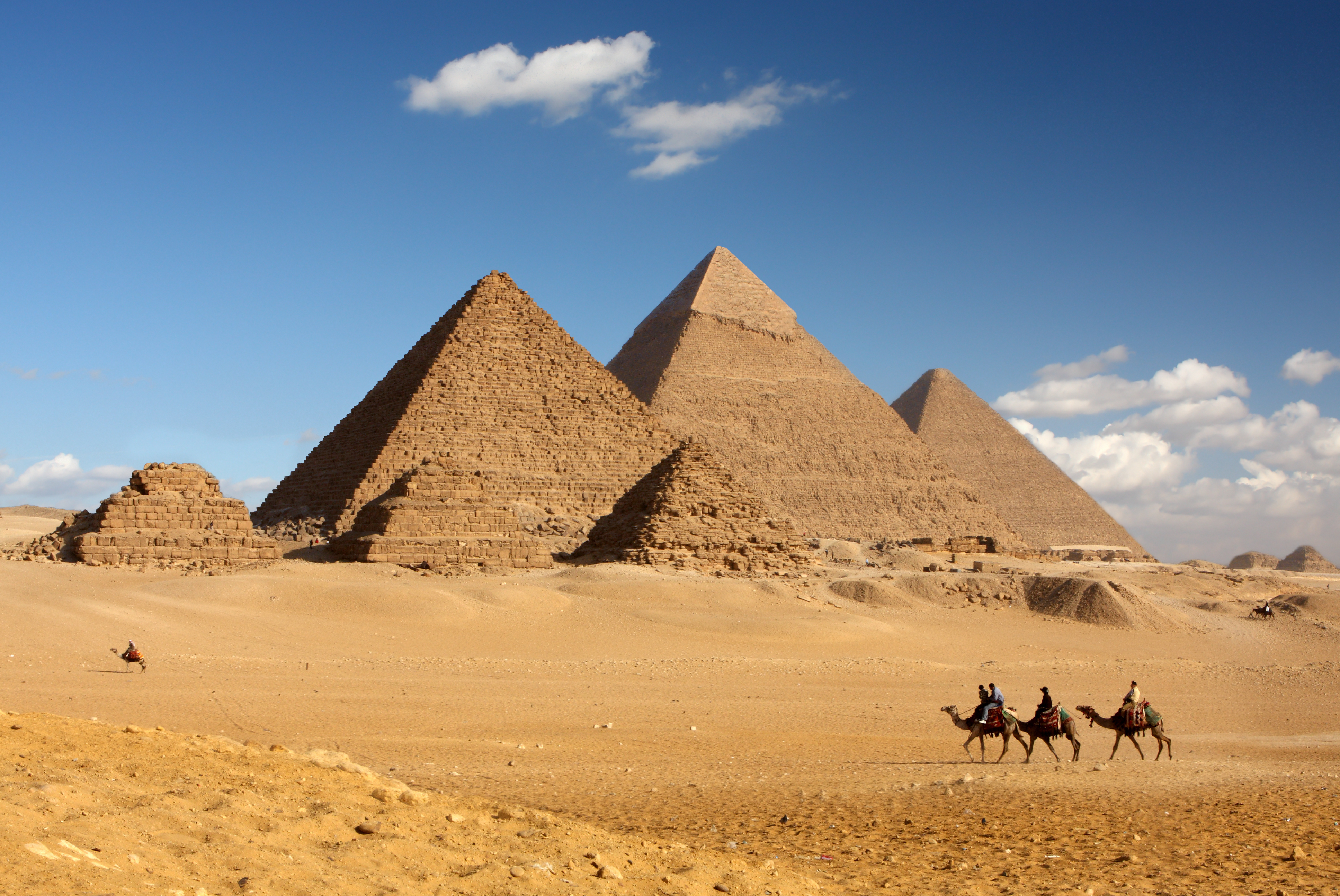 De tre store pyramider i Giza med en kamelkaravane, der krydser den golde ørken under en klar blå himmel i Egypten
