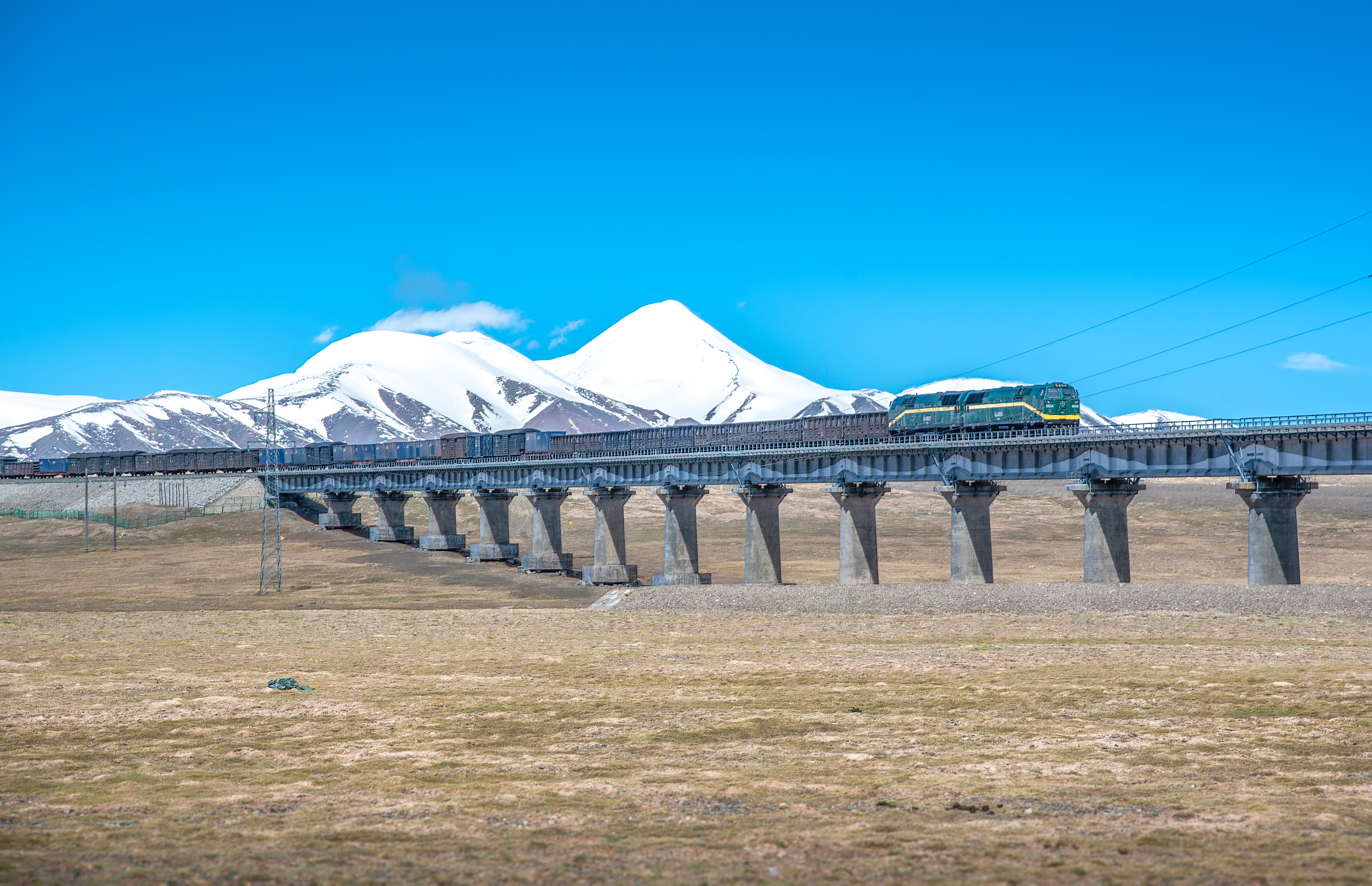 Passagertog på Qinghai-Tibet jernbanen krydser bro med snedækte Kunlun bjerge