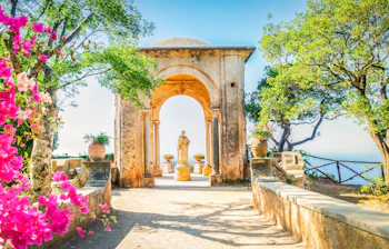 Smuk stenbue i Ravello landsby på Amalfikysten i Italien, omgivet af lyserøde bougainvillea blomster og grønne træer med udsigt over Middelhavet