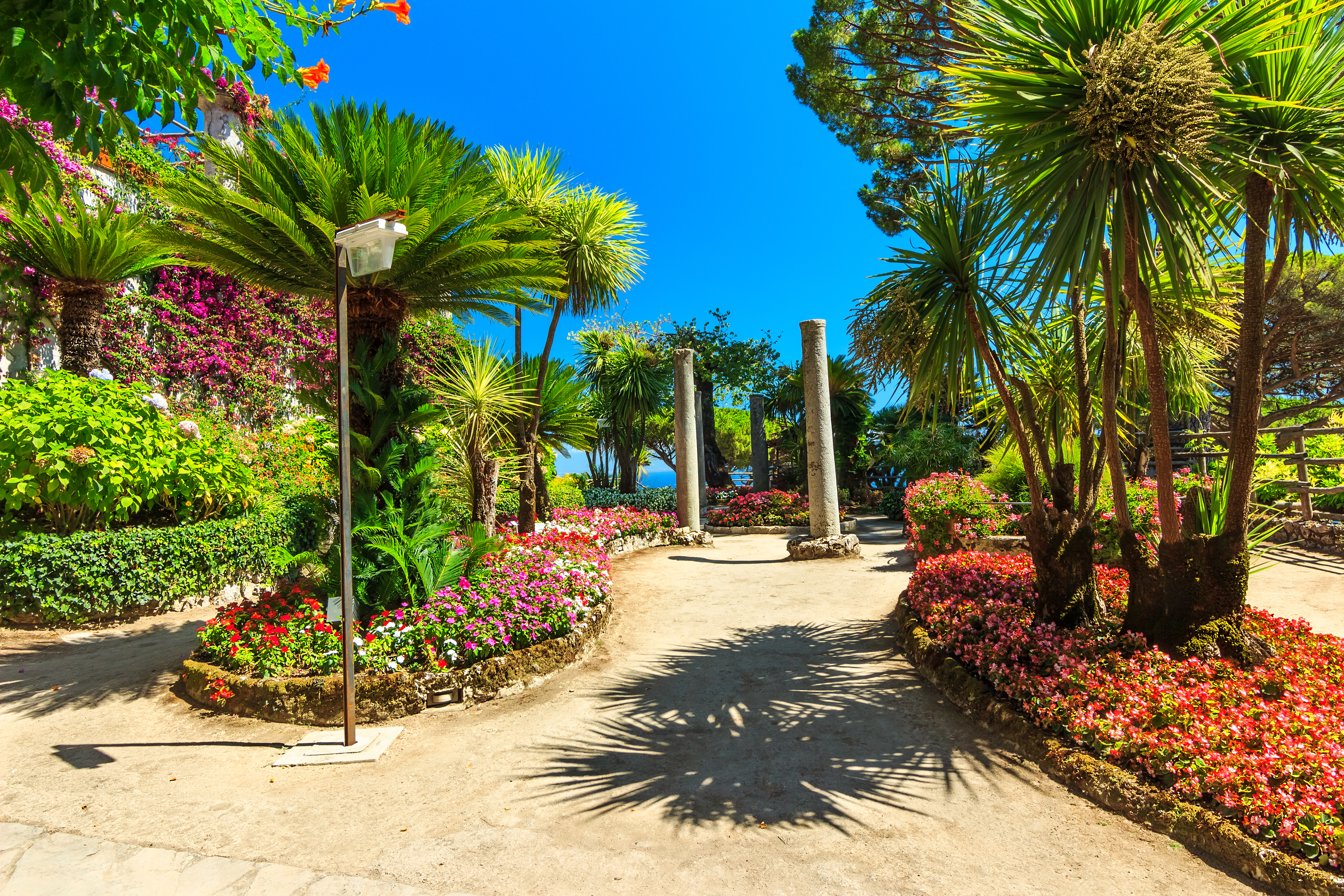 Betagende udsigt over en romantisk middelhavsblomsterhave med farverige blomster, elegante søjler og frodig grøn vegetation med udsigt over det azurblå hav fra Villa Rufolos terrasser i Ravello på Amalfikysten, Italien