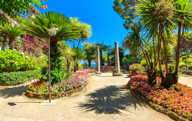 Betagende udsigt over en romantisk middelhavsblomsterhave med farverige blomster, elegante søjler og frodig grøn vegetation med udsigt over det azurblå hav fra Villa Rufolos terrasser i Ravello på Amalfikysten, Italien