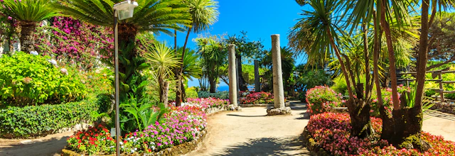 Betagende udsigt over en romantisk middelhavsblomsterhave med farverige blomster, elegante søjler og frodig grøn vegetation med udsigt over det azurblå hav fra Villa Rufolos terrasser i Ravello på Amalfikysten, Italien