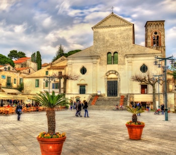 Den historiske Ravello Katedral med sit klokketårn på det livlige bytorv med palmer og caféer på Amalfikysten i Italien