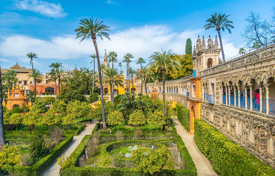 Smukke haver ved det kongelige Alcazar-palads i Sevilla med frodig vegetation, palmer og elegante stier - oplev den unikke blanding af maurisk og spansk arkitektur i dette UNESCO-verdensarvssted i Andalusien, Spanien