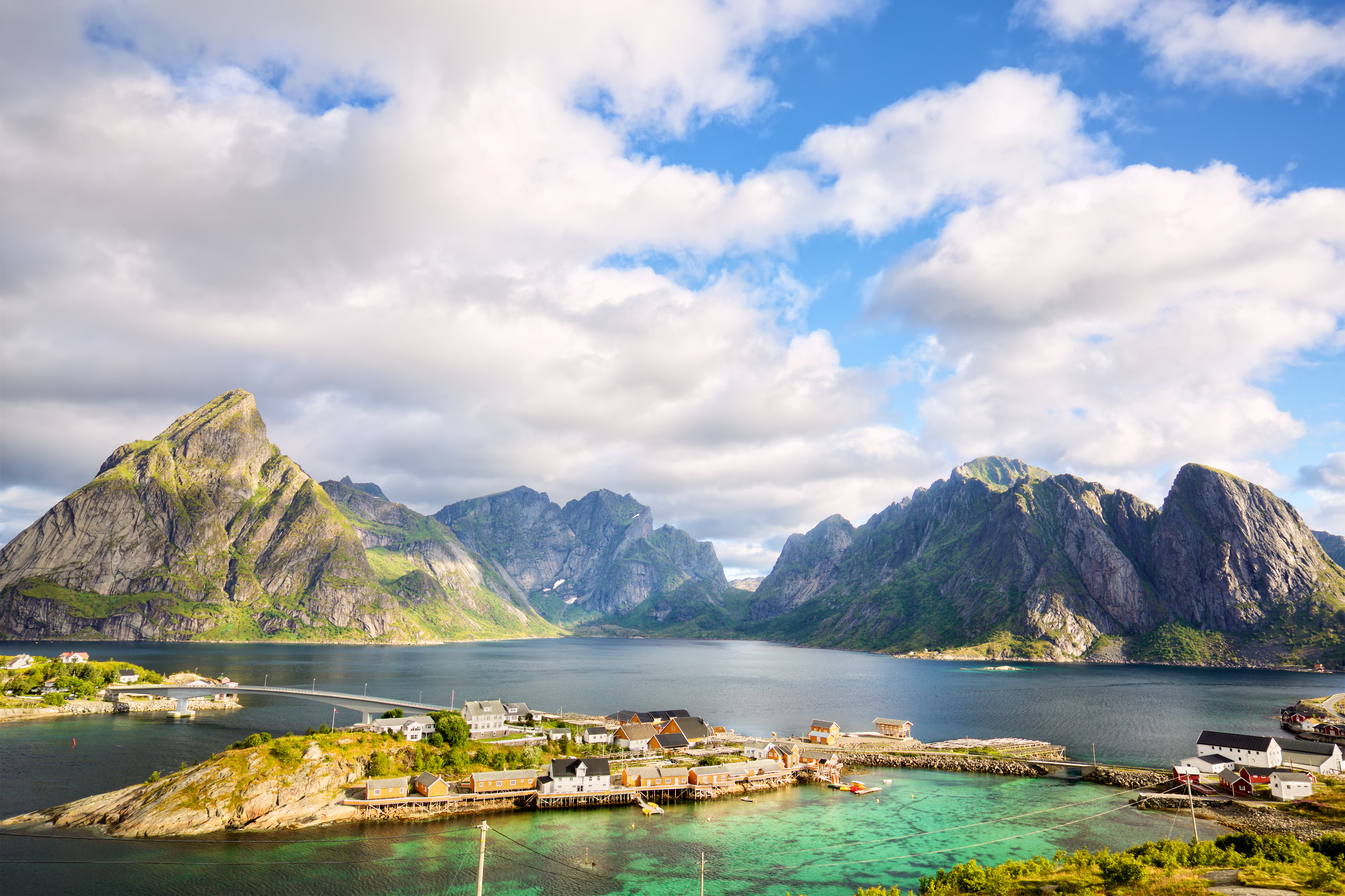 Malerisk udsigt over fiskerelandsbyen Reine på Lofoten i Norge med turkisblåt vand, traditionelle røde rorbuer og dramatiske bjergtinder