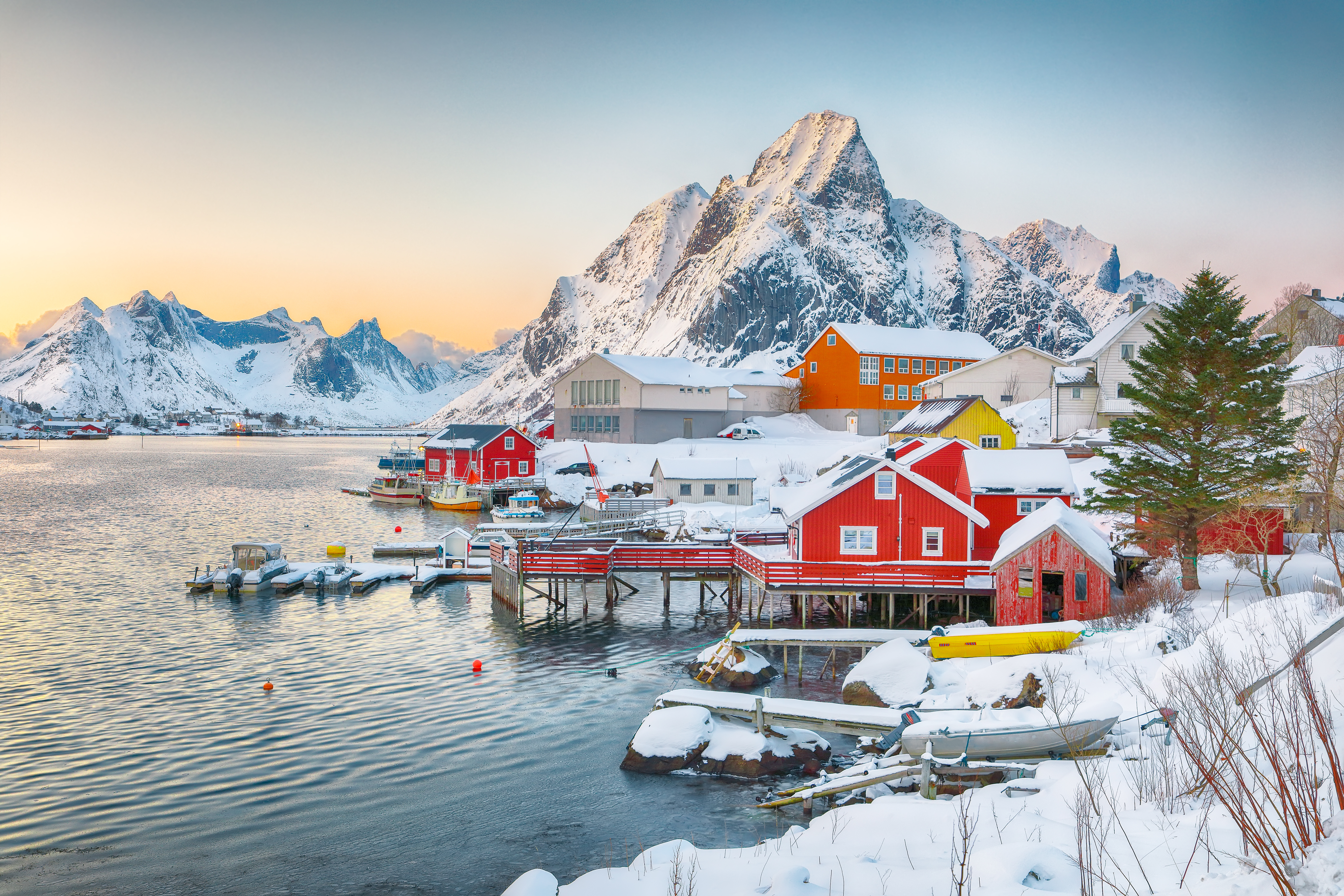 Malerisk aftenudsigt over røde rorbuer i Reine, Lofoten med bjerge spejlet i Reinefjorden, Norge