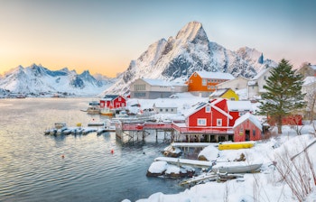 Malerisk aftenudsigt over røde rorbuer i Reine, Lofoten med bjerge spejlet i Reinefjorden, Norge