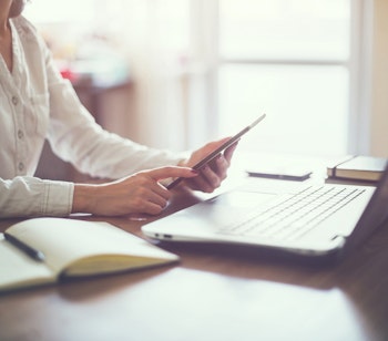 Rejseplanlægger arbejder ved skrivebord med laptop og tablet for at organisere rejsedetaljer i et lyst hjemmekontor