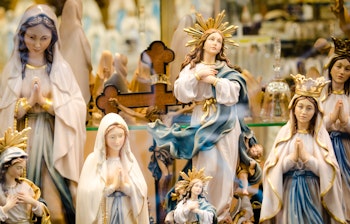 Katolske religiøse statuer og figurer af Jomfru Maria i en souvenirbutik i pilgrimsbyen Lourdes i Frankrig