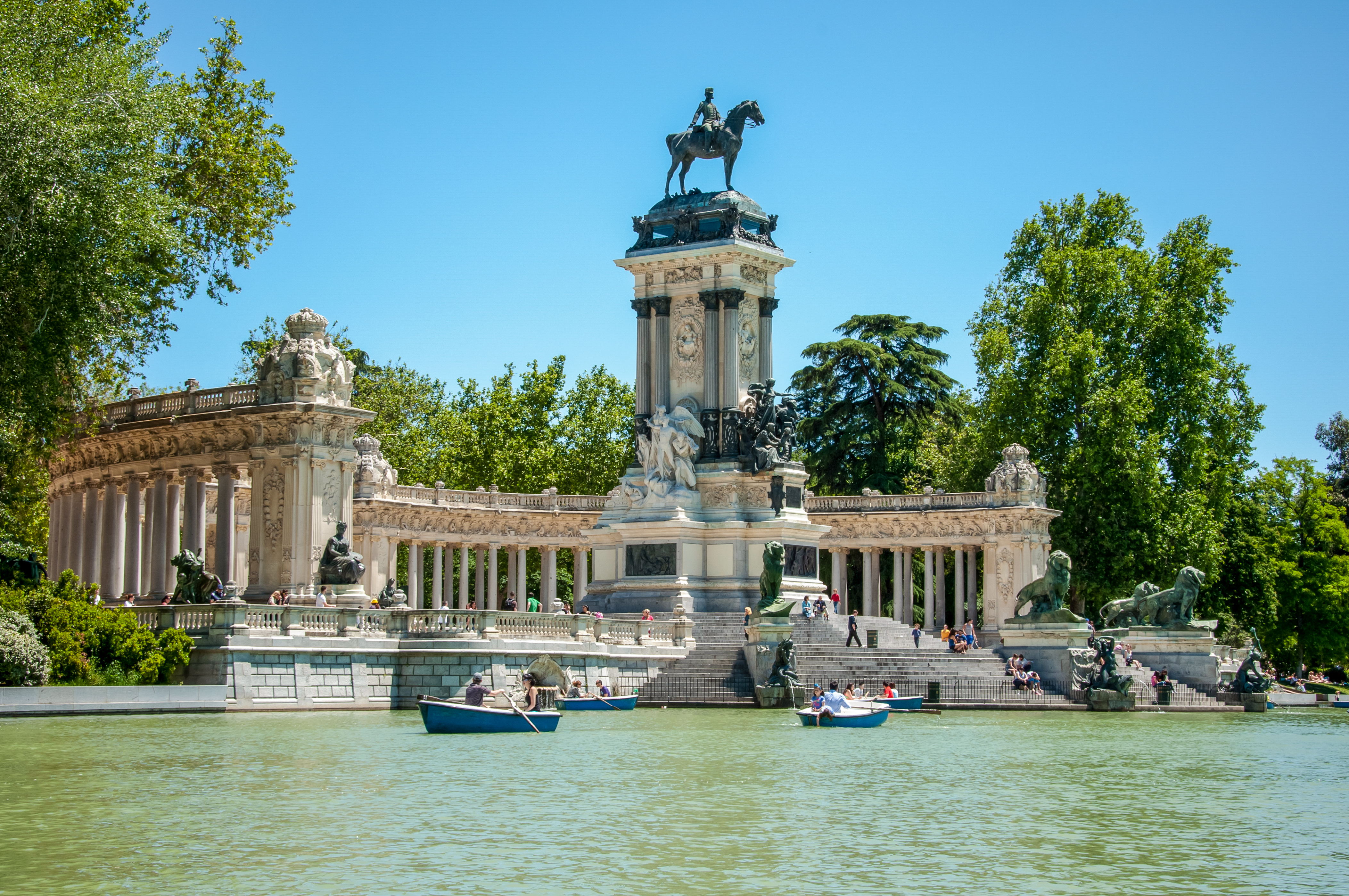 Det majestætiske Alfonso XII monument ved søen i Retiro Parken i Madrid med robåde og grønne omgivelser på en solrig dag