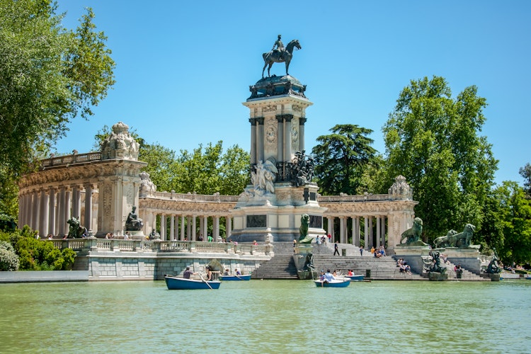 Det majestætiske Alfonso XII monument ved søen i Retiro Parken i Madrid med robåde og grønne omgivelser på en solrig dag