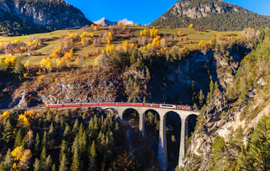 Rødt tog på det berømte Landwasser Viadukt omgivet af farverige efterårsfarvede træer i de schweiziske alper i Graubünden
