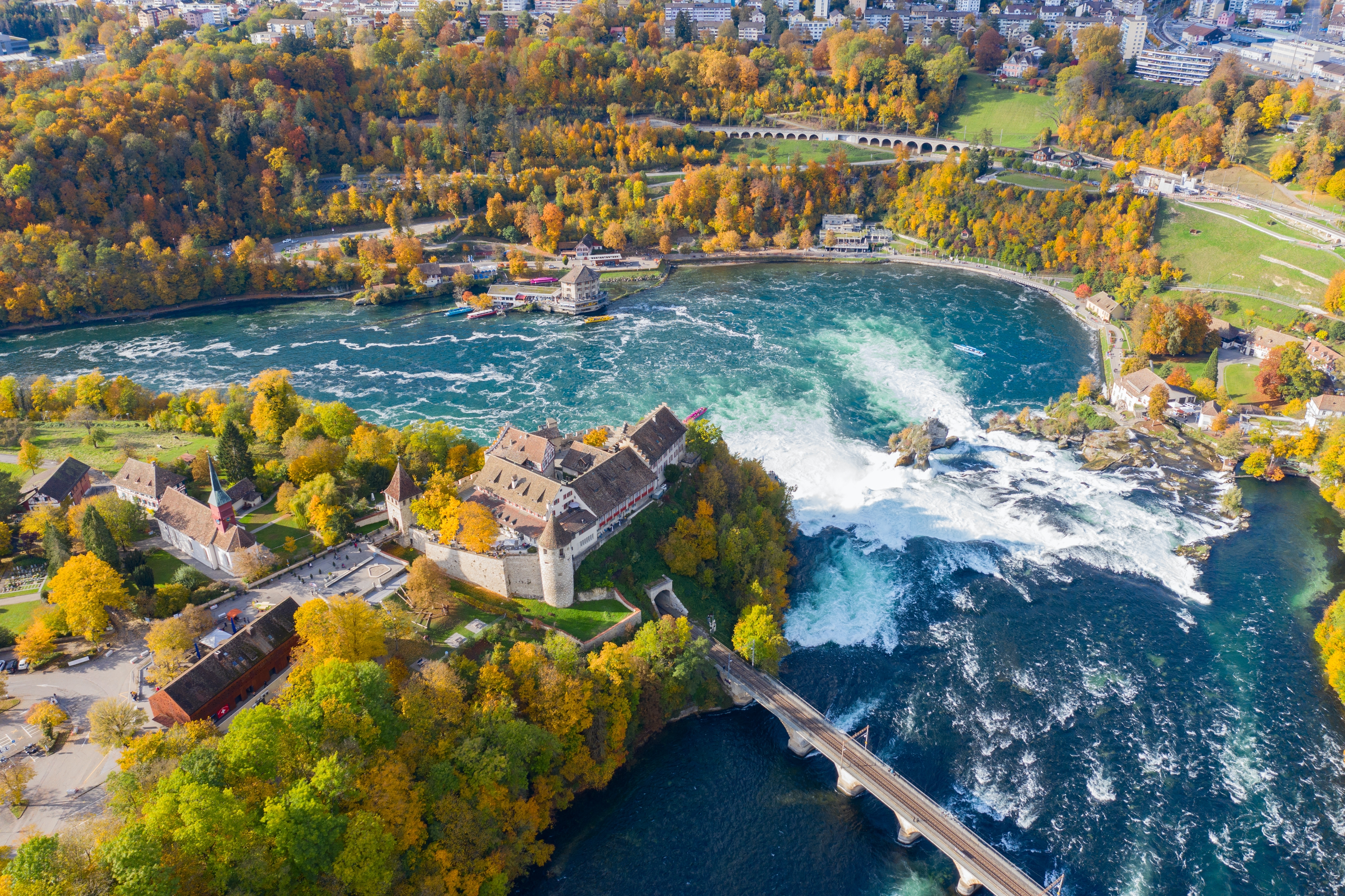 Luftfoto af Rhinfaldene ved Schaffhausen i Schweiz med Laufen Slot omgivet af farverig efterårsskov og turkisblåt vand