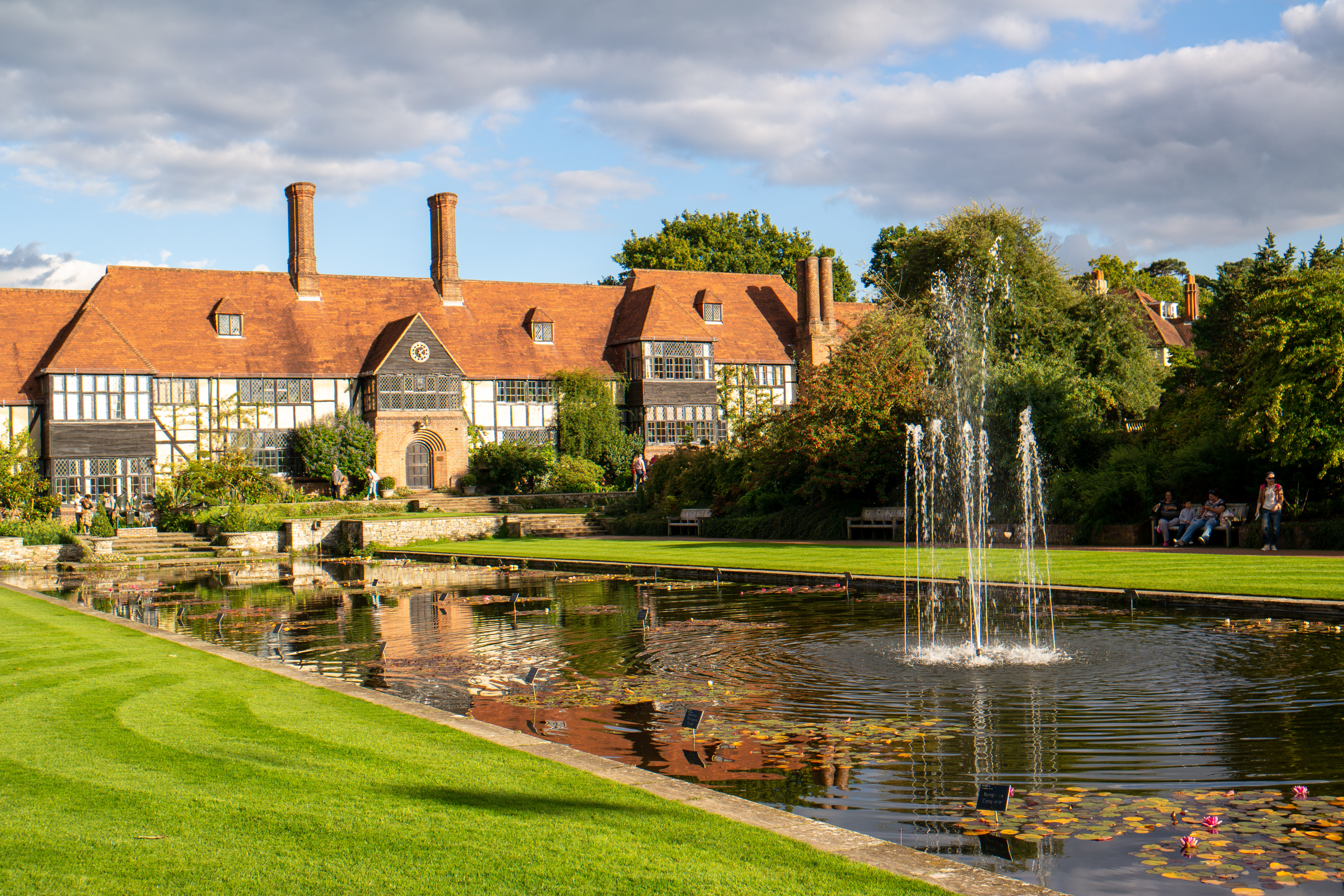 Den smukke RHS Wisley Have med springvand i lilje-dam og historisk Tudor-bygning omgivet af grønne plæner i Surrey, England