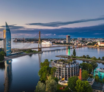 Rigas imponerende skyline ved solnedgang med moderne bygninger, historisk bymidte og den smukke Daugava-flod i forgrunden