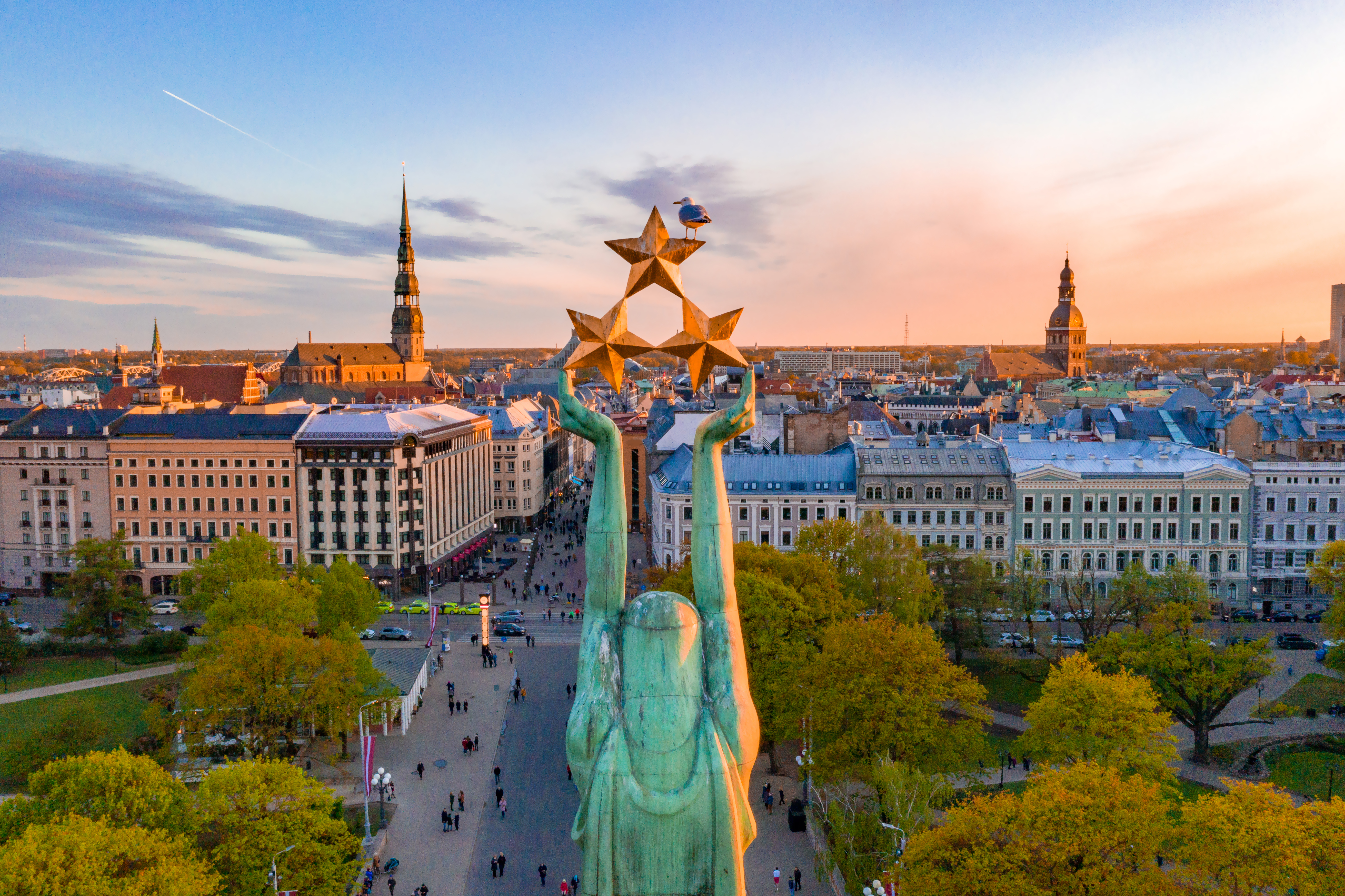 Luftfoto af Frihedsmonumentet i Riga med gyldne stjerner over den historiske gamle bydel ved solnedgang
