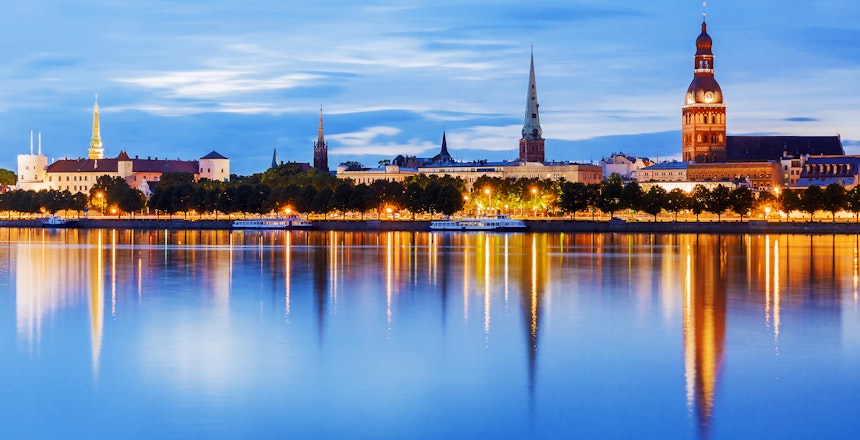 Betagende natpanorama af Rigas skyline med oplyste historiske bygninger og kirkespir, der spejler sig smukt i Daugava-floden i Letland