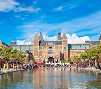 Det historiske Rijksmuseum i Amsterdam med det ikoniske I Amsterdam-skilt foran, som reflekteres i vandspejlet - et must-see på din rejse til Holland
