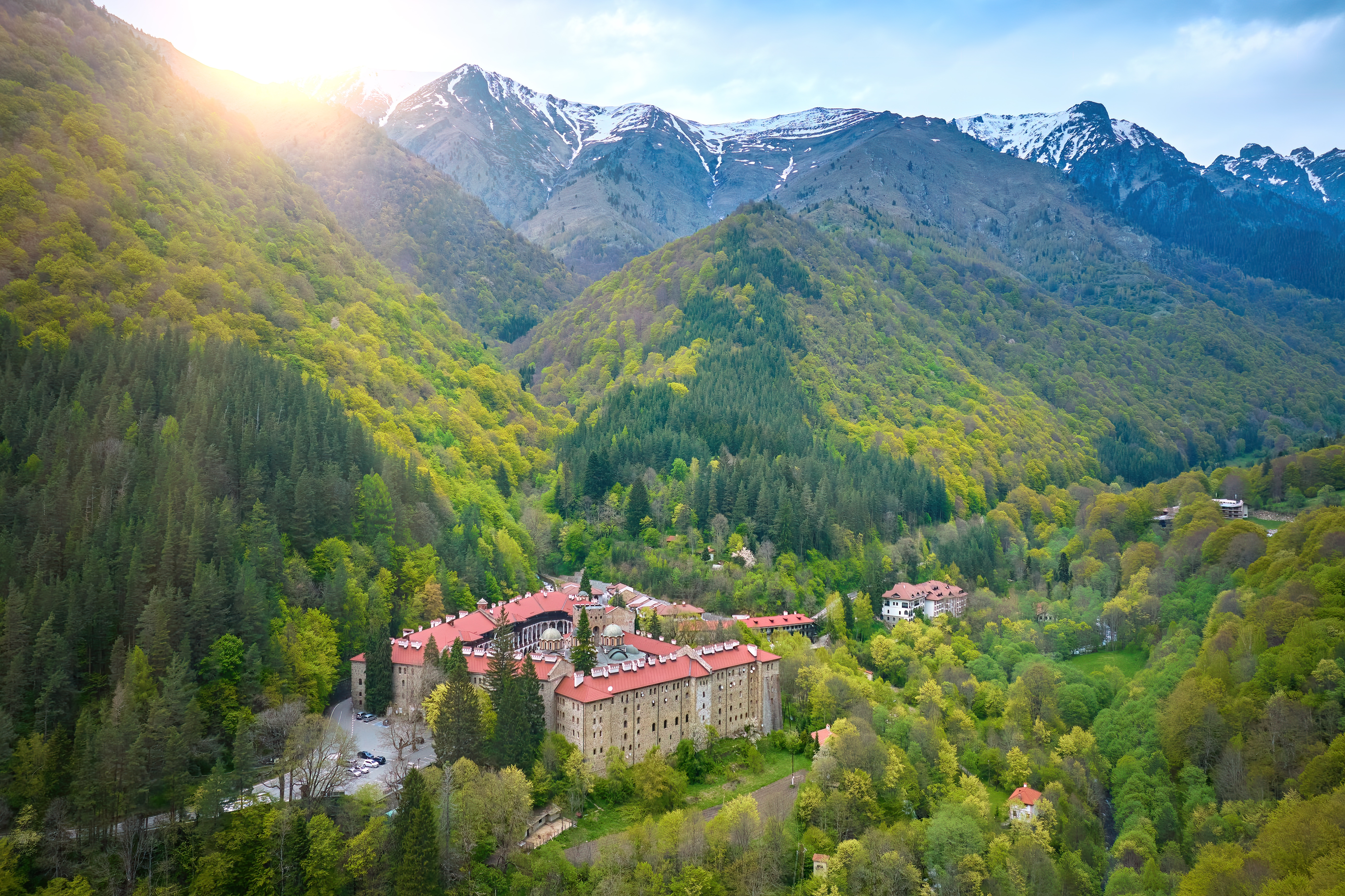 Historisk Rila Kloster i de bulgarske bjerge med sne-toppede toppe og forårsgrönt