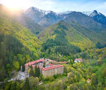 Historisk Rila Kloster i de bulgarske bjerge med sne-toppede toppe og forårsgrönt