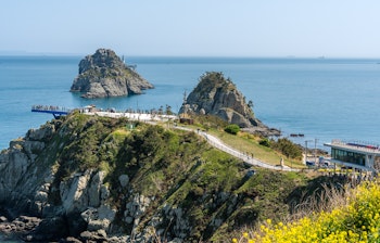 Rødt fyrtårn på den koreanske kyst ved solnedgang med roligt hav og skyer, der spejler sig i vandet